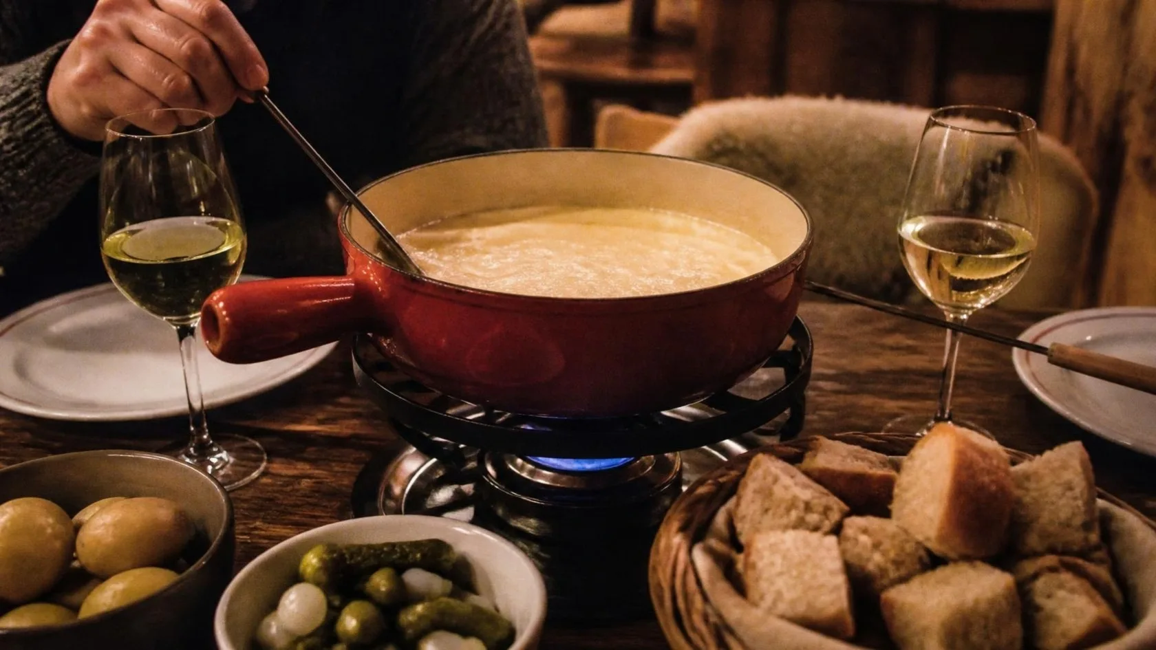 Käsefondue im Caquelon mit Brot, Kartoffeln und Essiggurken
